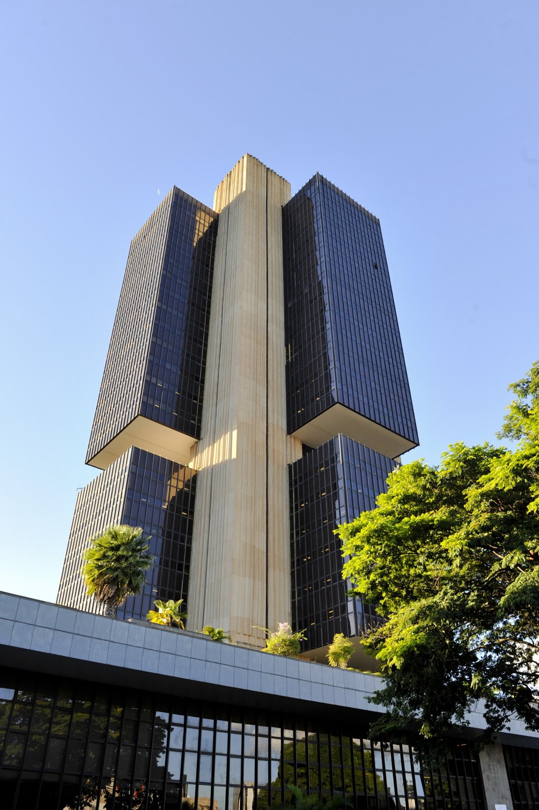 Sede do Banco Central em Brasília vista de baixo, com torre de vidro azul e palmeiras