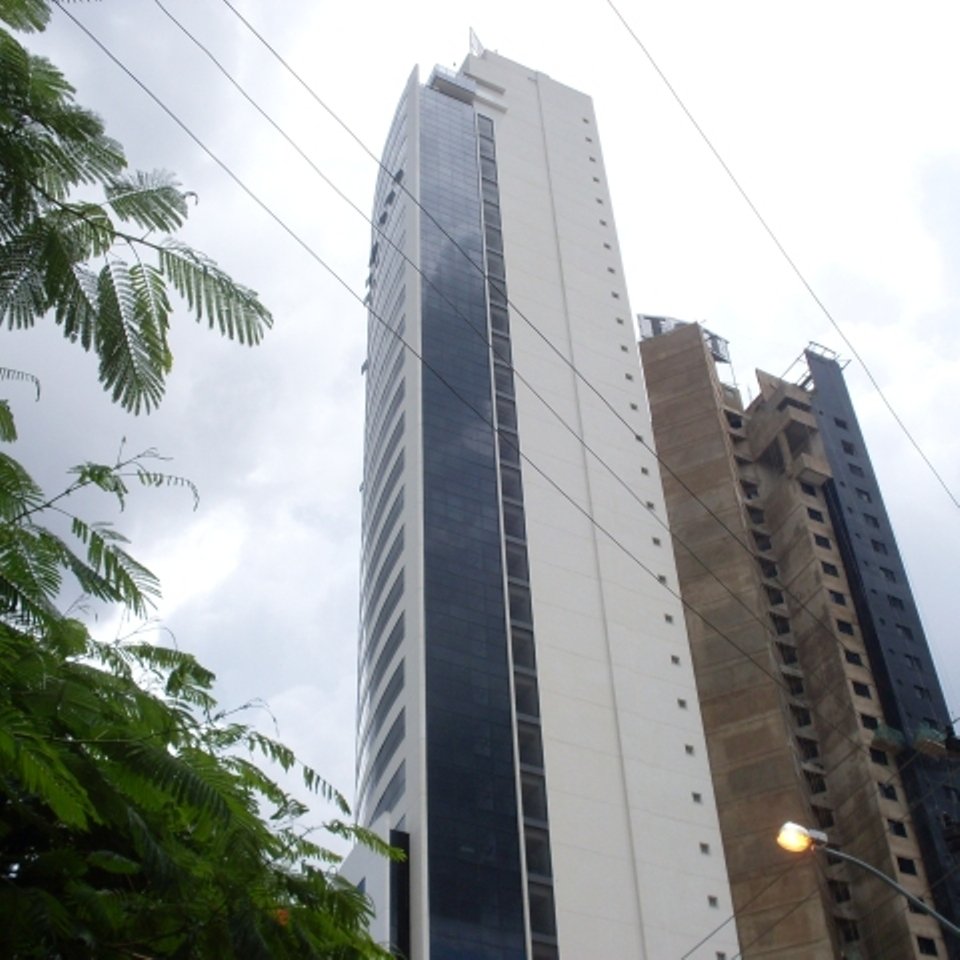 Edifício comercial em construção em Goiânia, visto de baixo, com fiação e árvores em primeiro plano