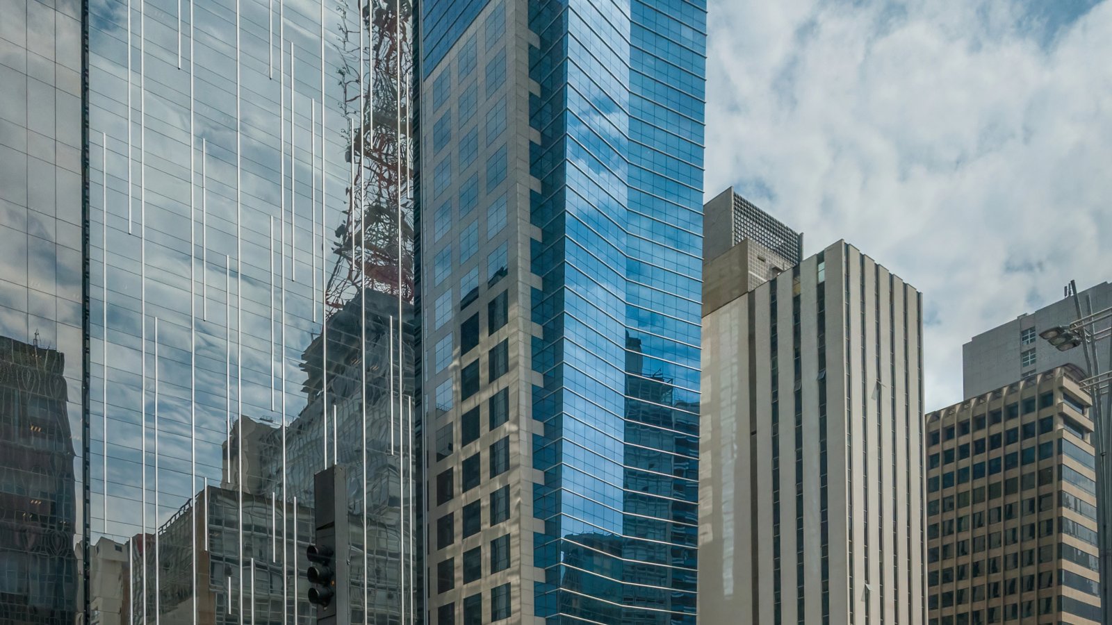 Fachada de edifícios comerciais espelhados na Avenida Paulista, em São Paulo, com céu nublado ao fundo